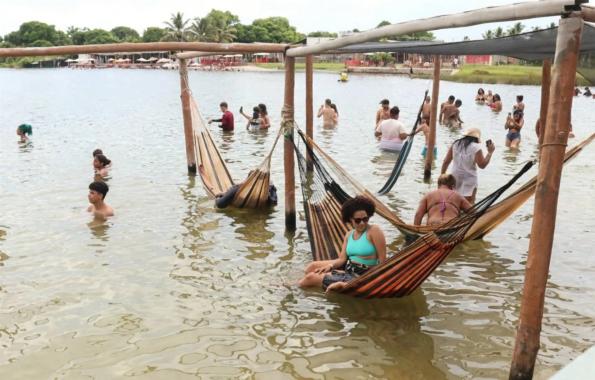 Redários suspensos sobre as águas cristalinas da Lagoa dos Tambaquis no Paraíso dos Tambaquis em Estância, Sergipe, com banhistas relaxando em redes à beira da lagoa