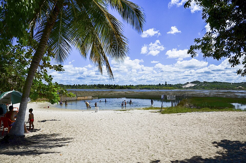 Praia de areia branca da Lagoa dos Tambaquis em Estância, Sergipe, com coqueiros, banhistas e a área de banho sinalizada do Paraíso dos Tambaquis
