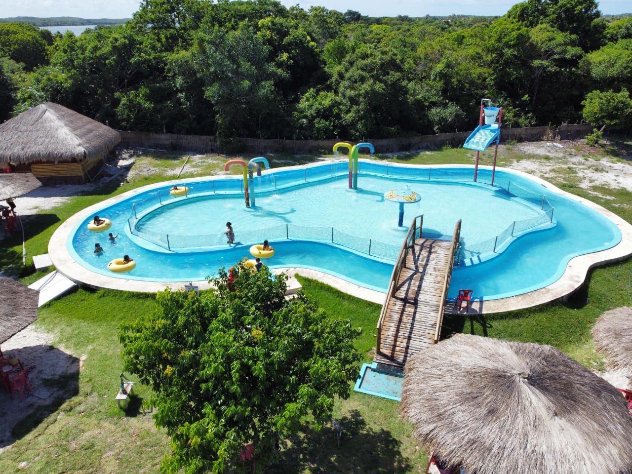 Vista aérea da piscina da Lagoa dos Tambaquis em Estância, Sergipe, com deck de madeira, boias e água cristalina cercada por coqueiros e natureza no Paraíso dos Tambaquis